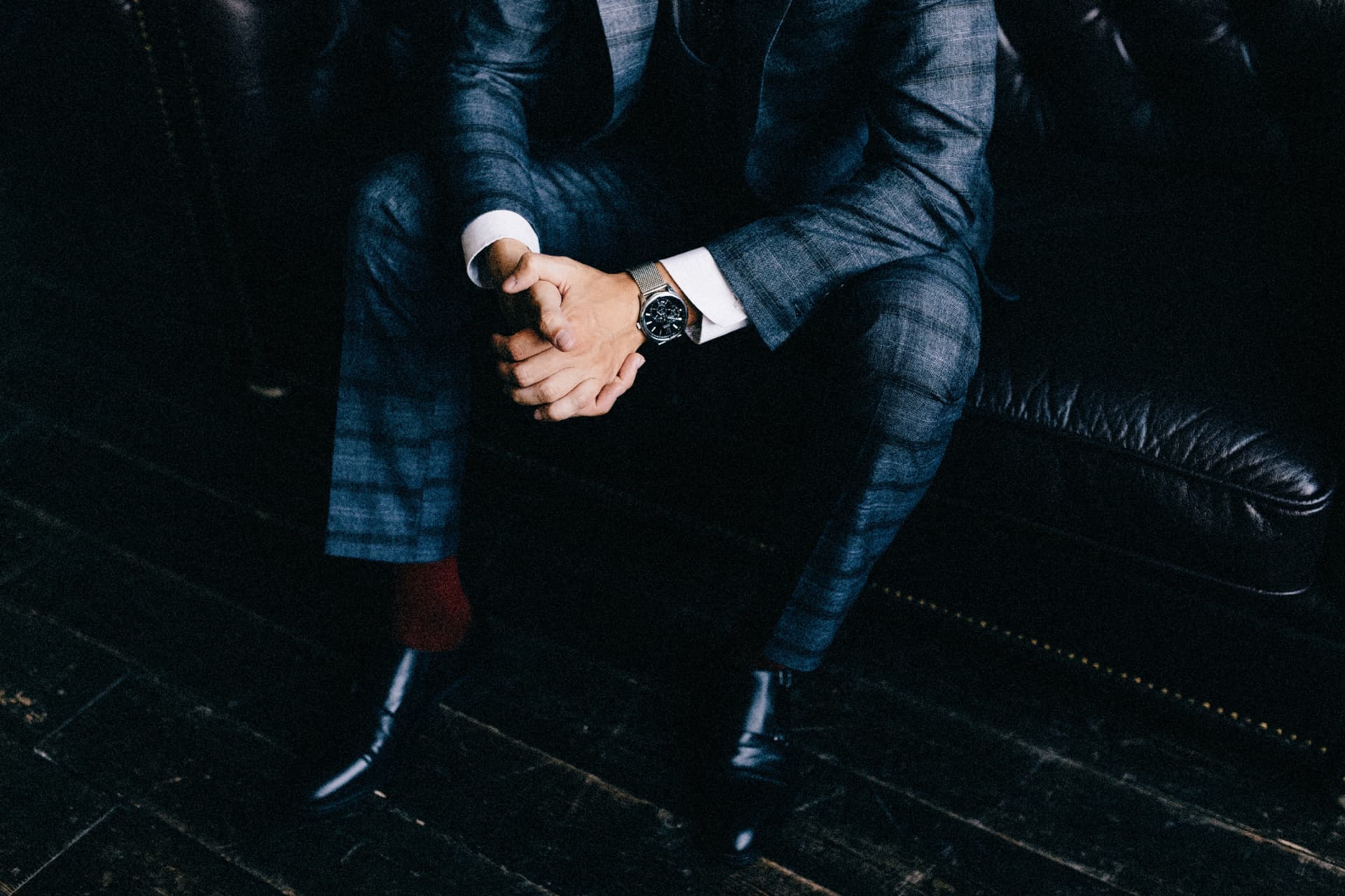 Chronograph on a mesh bracelet worn with a checked suit in a dark leather armchair